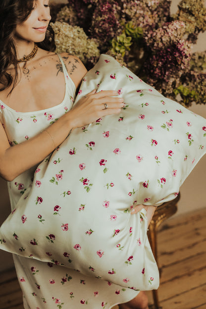 A woman in a matching white twill slip dress holds a large butter-yellow color pillow with a pink and green floral print.