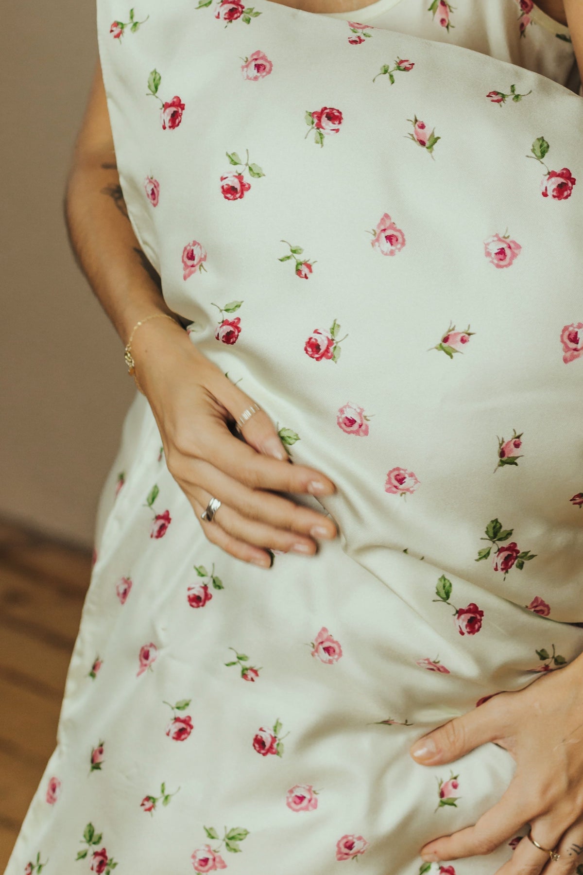 A woman  holds a large matching pillow against her torso. The pillow  feature a delicate pink and red floral print on an butter-yellow twill fabric.