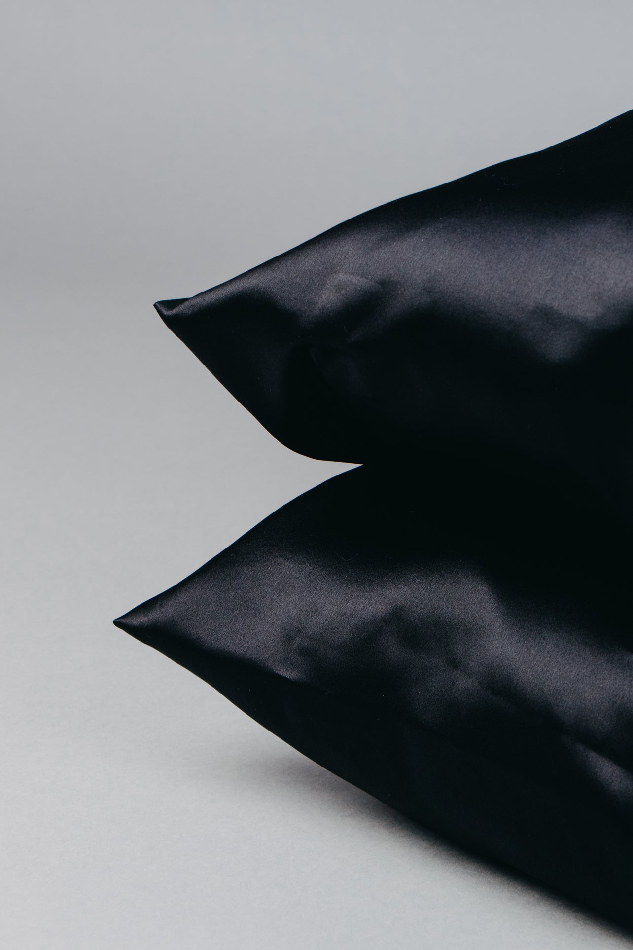 two black pillows with silk pillowcases one on top of other, pillow corners