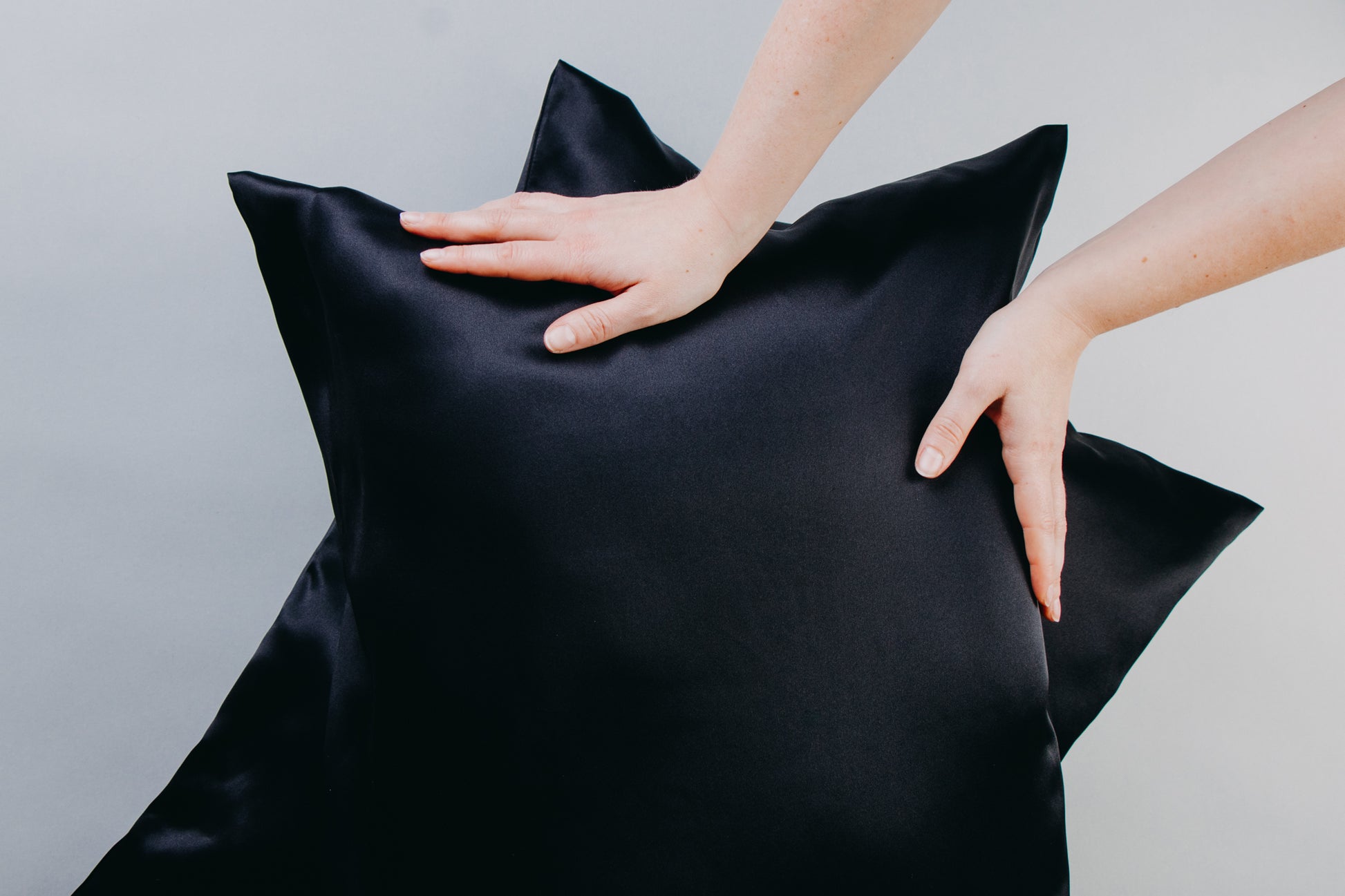 hands holding two black pillows with silk pillowcases