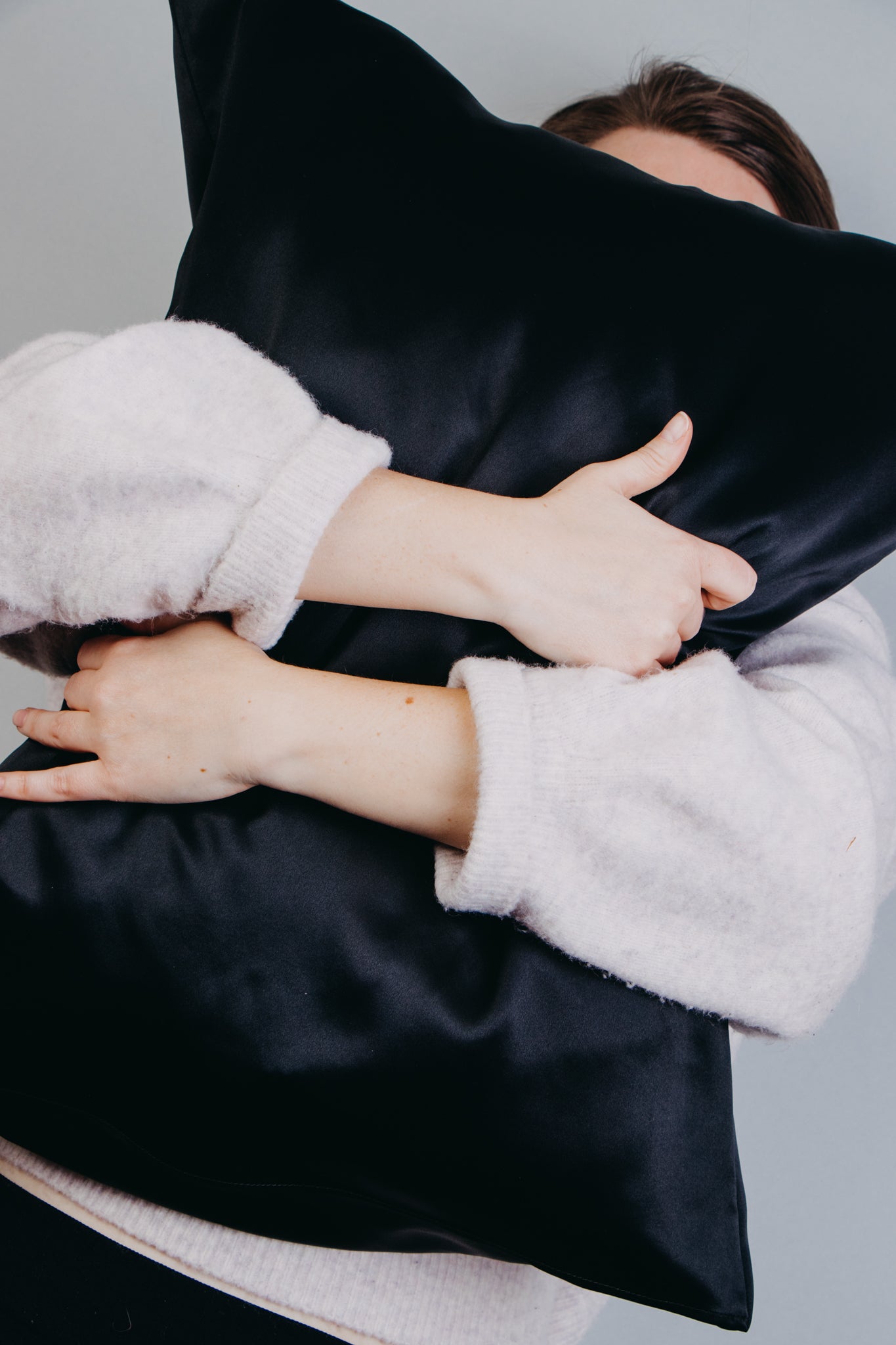 Black silk pillowcase, hands around and holding black pillow